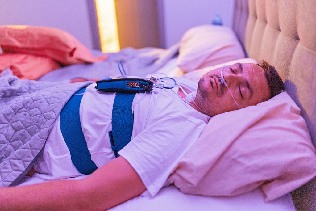 Un homme dort dans un lit, connecté à des machines qui évaluent sa condition lors du service de tests de sommeil.